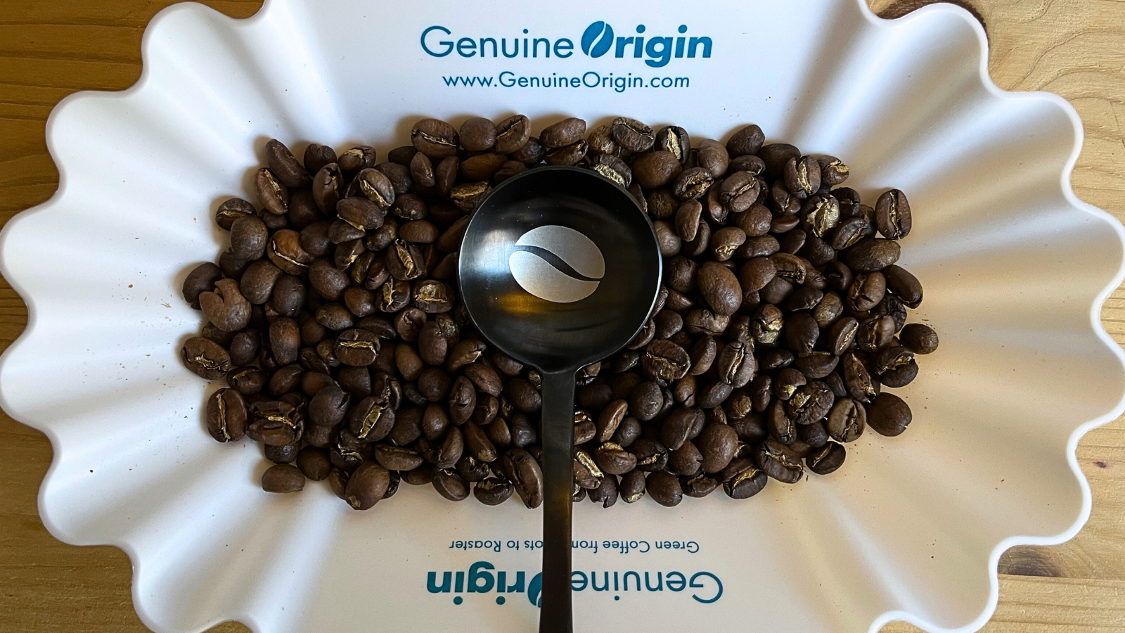 Custom Genuine Origin matte black coffee cupping spoon in white Genuine Origin coffee cupping tray resting on fresh roasted coffee